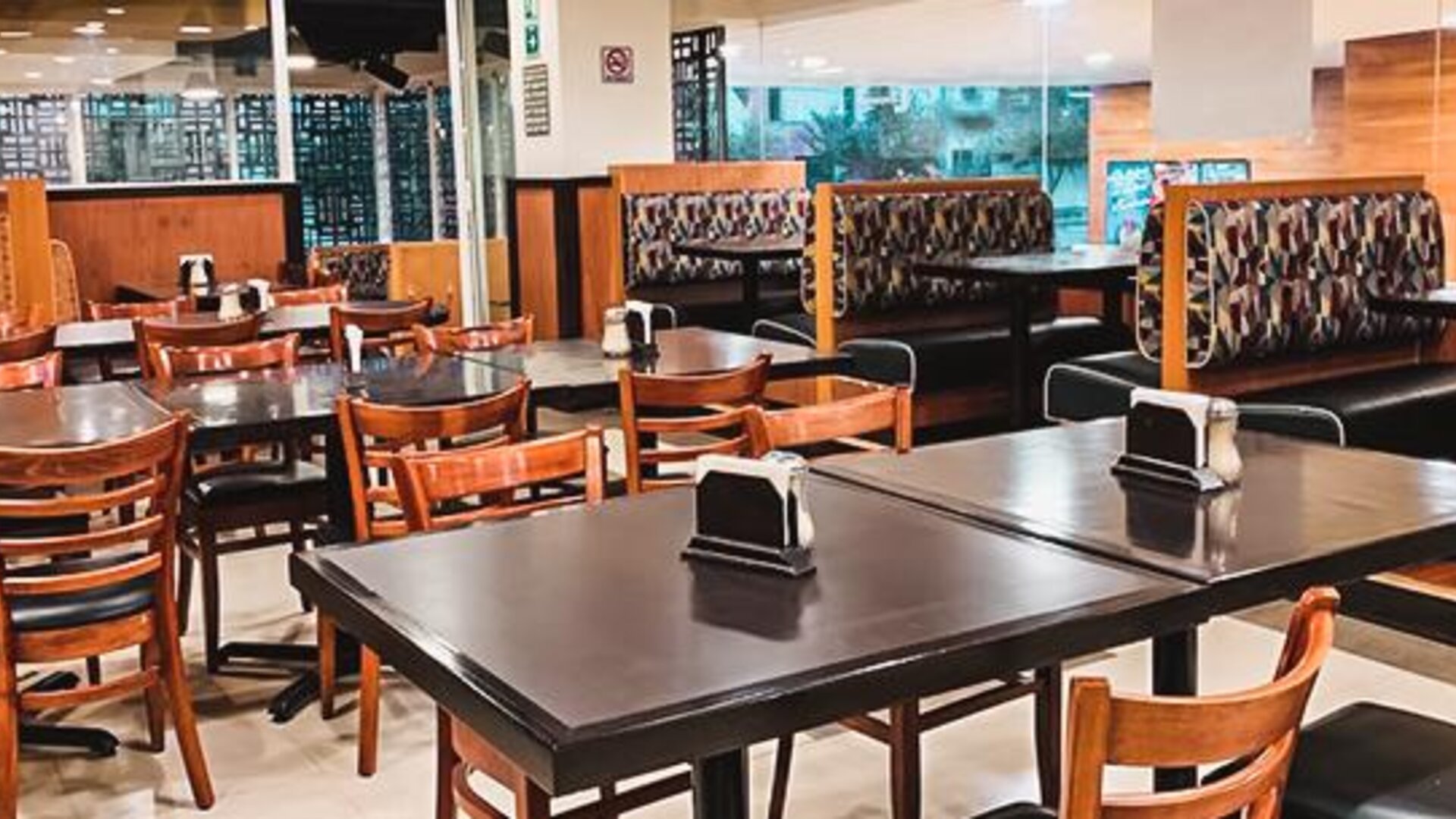 Restaurant seating area with wooden tables, upholstered booths and large windows overlooking the street at Hotel Lepanto.