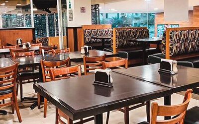 Restaurant seating area with wooden tables, upholstered booths and large windows overlooking the street at Hotel Lepanto.