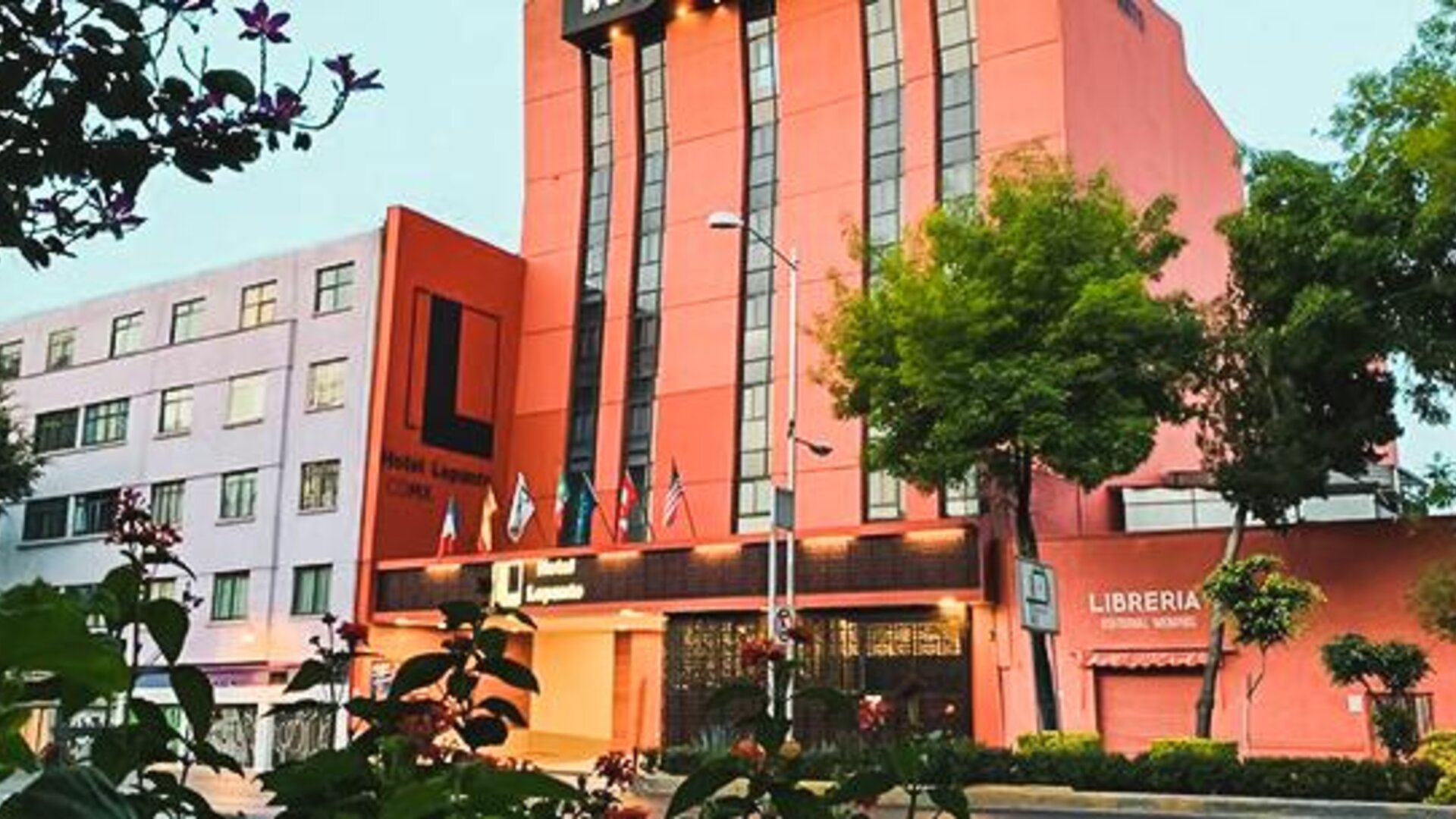 Hotel exterior with entrance, flags and landscaped trees along the surrounding city street at Hotel Lepanto.