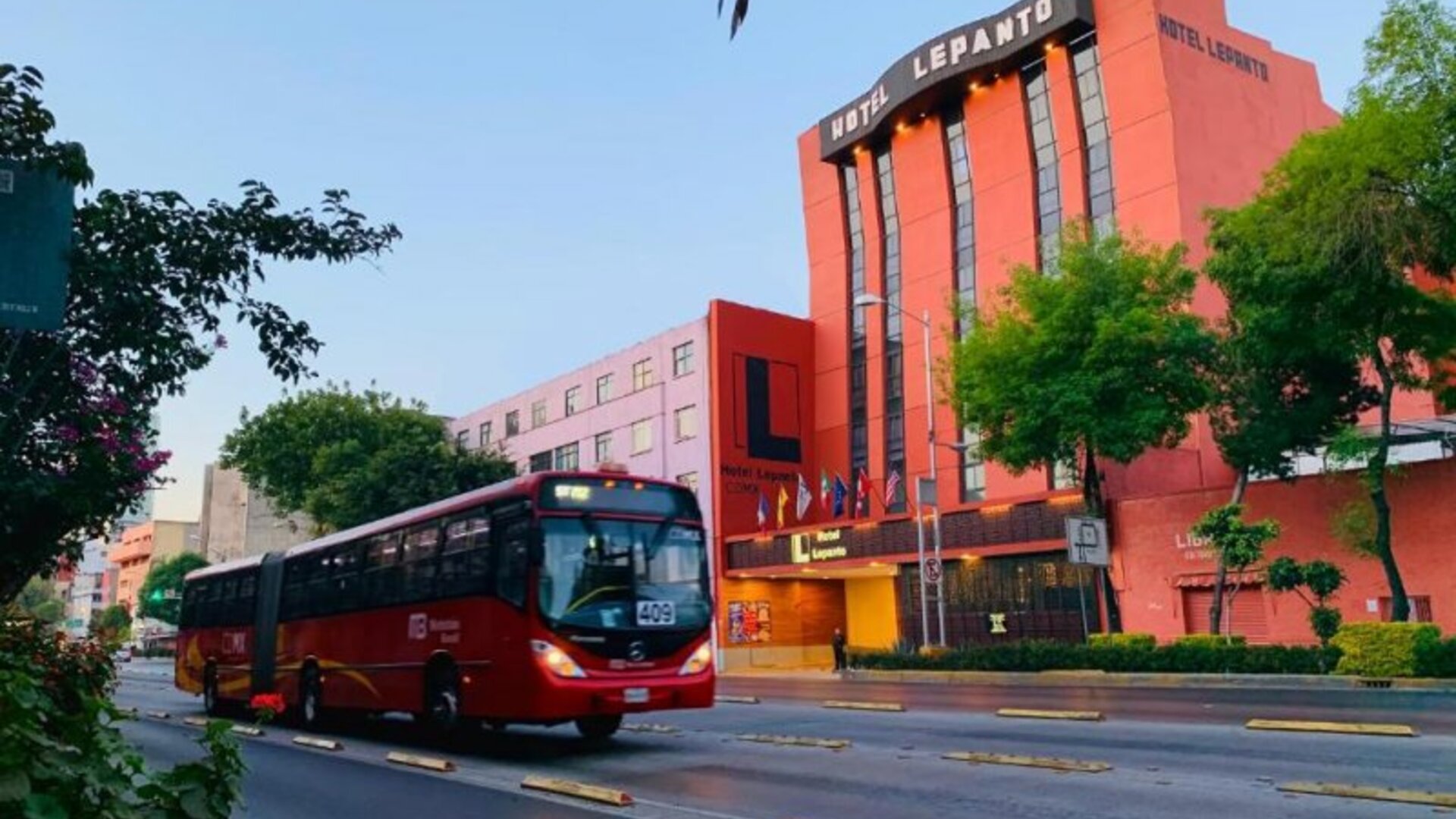 Hotel exterior with prominent signage viewed from a tree-lined street and passing city bus at Hotel Lepanto.