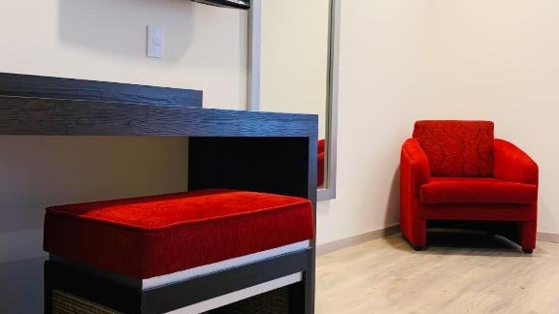 Guest room seating area with wall-mounted TV, full-length mirror and red upholstered chairs at Hotel Lepanto.
