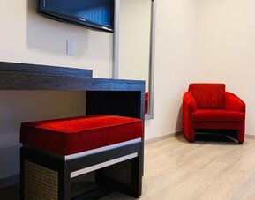 Guest room seating area with wall-mounted TV, full-length mirror and red upholstered chairs at Hotel Lepanto.