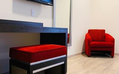 Guest room seating area with wall-mounted TV, full-length mirror and red upholstered chairs at Hotel Lepanto.