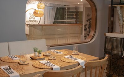 Contemporary dining area with wooden tables, woven placemats and views of the reception area at Marbore Hotel & Spa.