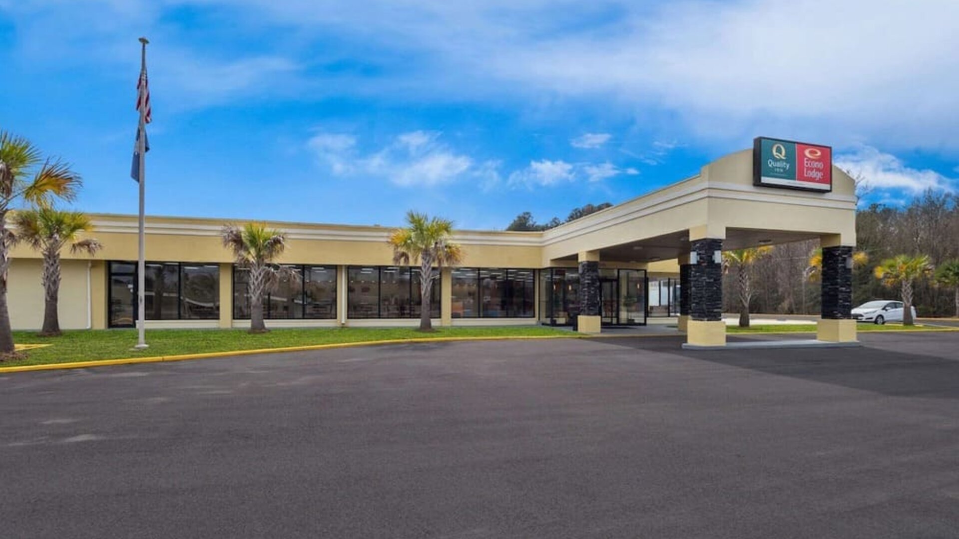 Hotel exterior with covered entrance, palm trees and parking area beneath a blue sky at Quality Inn Yemassee - Point South I-95.
