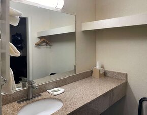 Bathroom vanity with granite countertop, large mirror, open shelving and hanging space at Econo Lodge Yemassee.