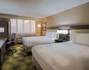 Guest room with two queen beds, HDTV, workspace, blackout curtains, and modern furnishings for a comfortable stay.