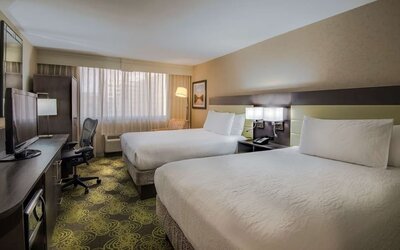 Guest room with two queen beds, HDTV, workspace, blackout curtains, and modern furnishings for a comfortable stay.