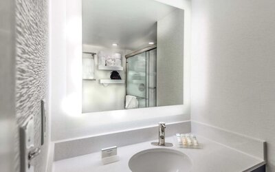 Modern guest bathroom with illuminated vanity mirror, spacious countertop, walk-in shower, and premium bath amenities.