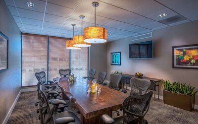 Private meeting room with large conference table, ergonomic chairs, TV, and natural light for business gatherings.