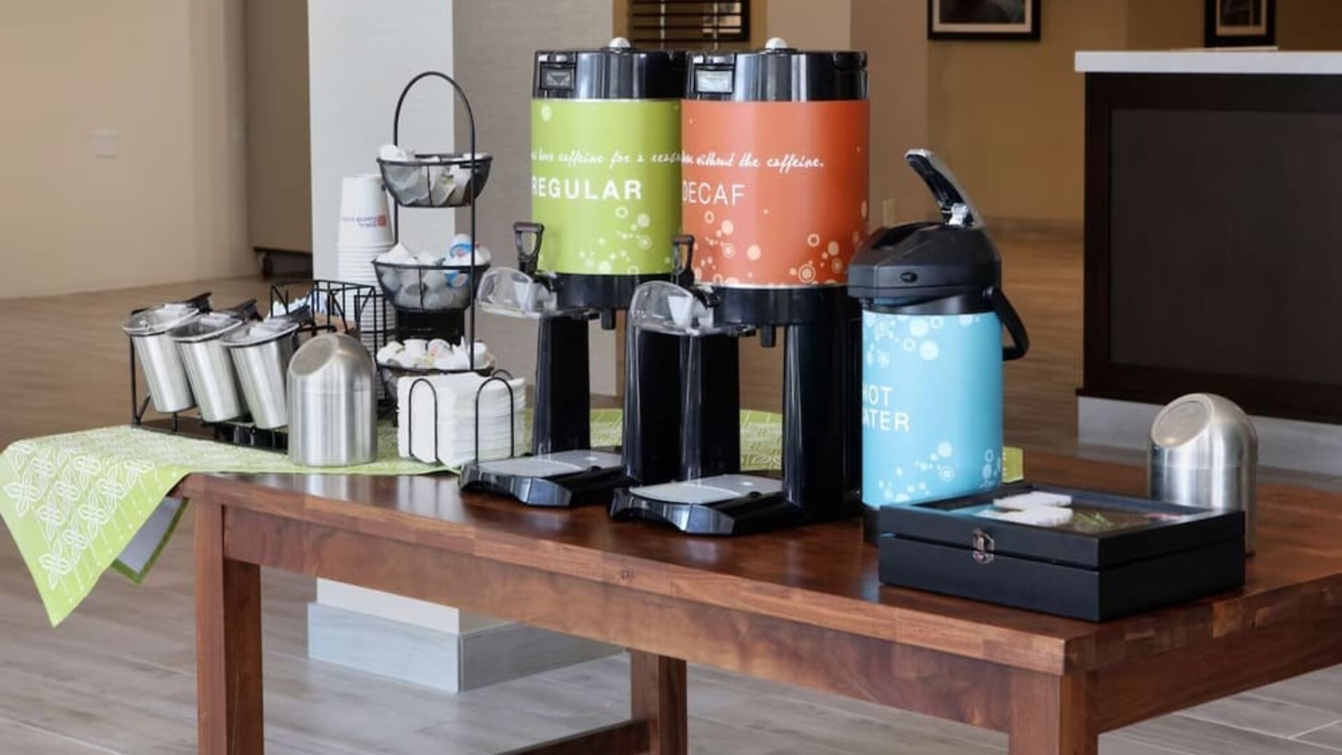 Complimentary coffee station featuring regular and decaf coffee, hot water, tea supplies, and condiments in the hotel lobby.