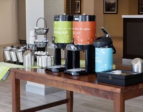 Complimentary coffee station featuring regular and decaf coffee, hot water, tea supplies, and condiments in the hotel lobby.
