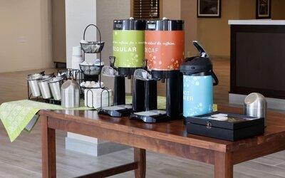 Complimentary coffee station featuring regular and decaf coffee, hot water, tea supplies, and condiments in the hotel lobby.