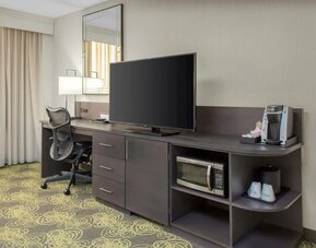 Guest room featuring a large HDTV, ergonomic desk, coffee maker, microwave, and workspace for business travelers.