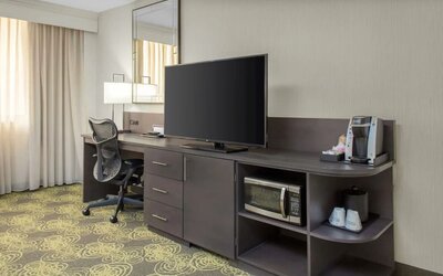 Guest room featuring a large HDTV, ergonomic desk, coffee maker, microwave, and workspace for business travelers.