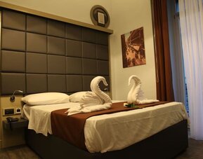 Cozy double guest room with plush bedding, decorative towel swans and natural light at Dolce Vita Rooms & Breakfast.