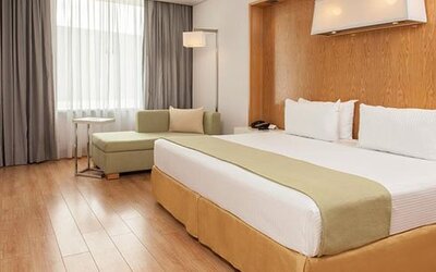 Bright guest room with king bed, chaise lounge, large windows and modern décor at NH Collection Mexico City Airport T2.