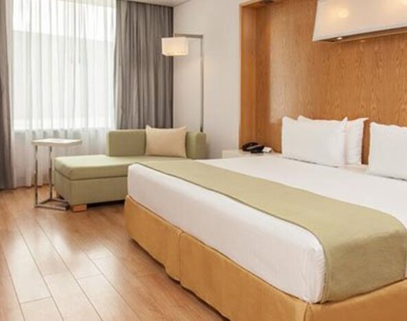 Bright guest room with king bed, chaise lounge, large windows and modern décor at NH Collection Mexico City Airport T2.