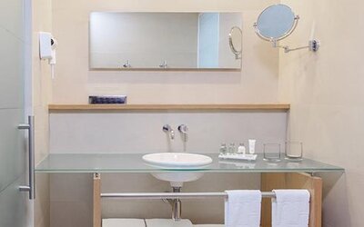 Contemporary bathroom with glass vanity, large mirror and complimentary bath amenities at NH Collection Mexico City Airport T2.