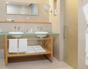 Modern bathroom with double vanity, bathtub, glass countertop and premium bath amenities at NH Collection Mexico City Airport T2.