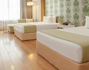 Spacious guest room with two double beds, seating area, large windows and modern décor at NH Collection Mexico City Airport T2.