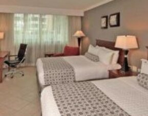 Spacious guest room with two double beds, work desk, lounge chair and large window at Crowne Plaza Panama.
