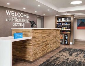 Hotel reception area with front desk, grab-and-go market and welcoming lobby at Hampton Inn Chicago O'Hare.
