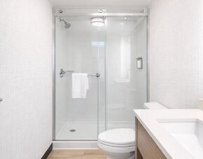 Contemporary guest bathroom with a walk-in glass shower, modern vanity, illuminated mirror and fresh towels at Hyatt Select Philadelphia Airport.