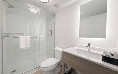 Contemporary guest bathroom featuring a walk-in glass shower, modern vanity, illuminated mirror and fresh towels at Hyatt Select Philadelphia Airport.