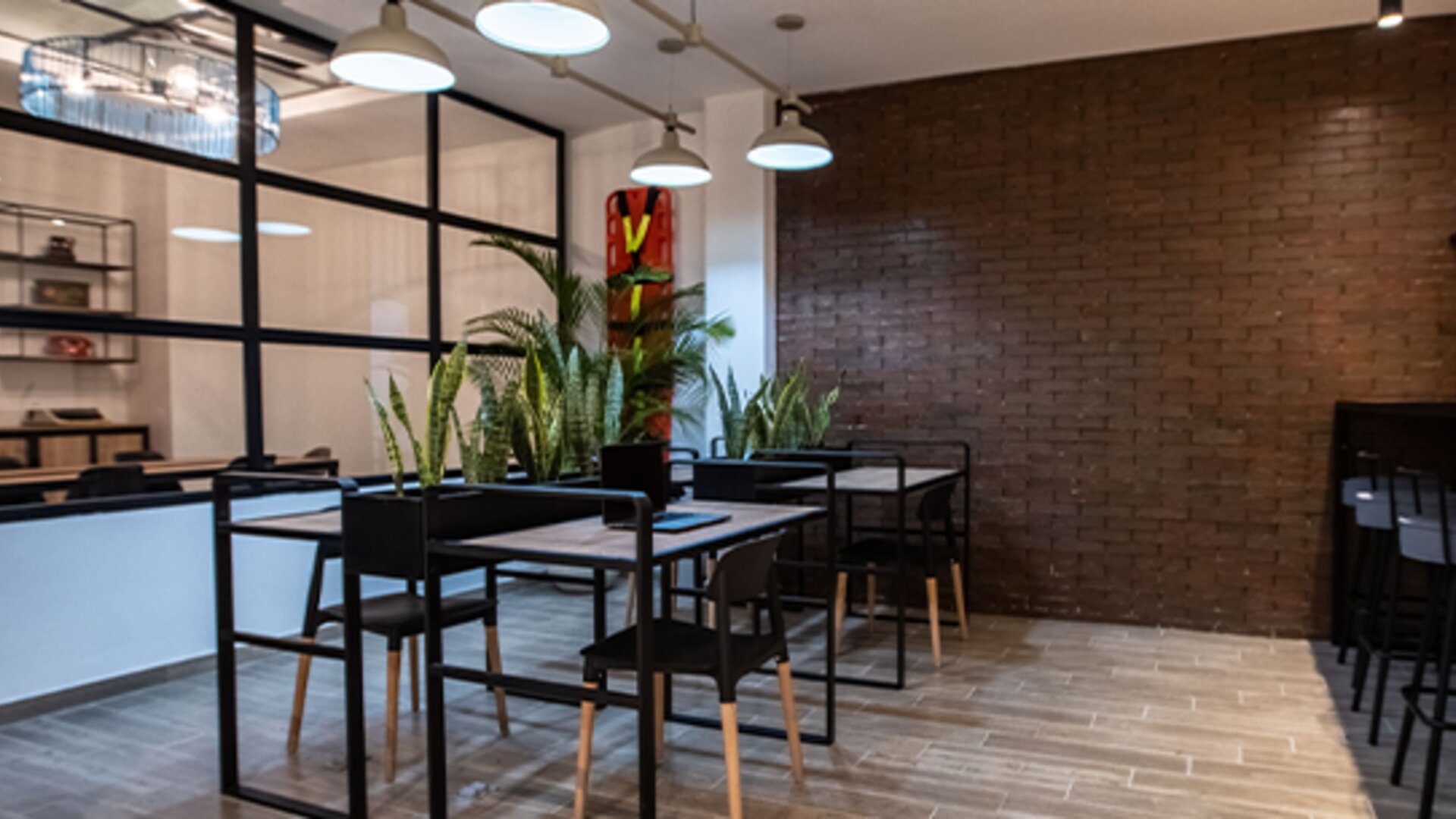 Communal dining area at 103 Wonderful House featuring modern tables, bar seating, indoor plants and exposed brick accents.