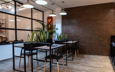 Communal dining area at 103 Wonderful House featuring modern tables, bar seating, indoor plants and exposed brick accents.