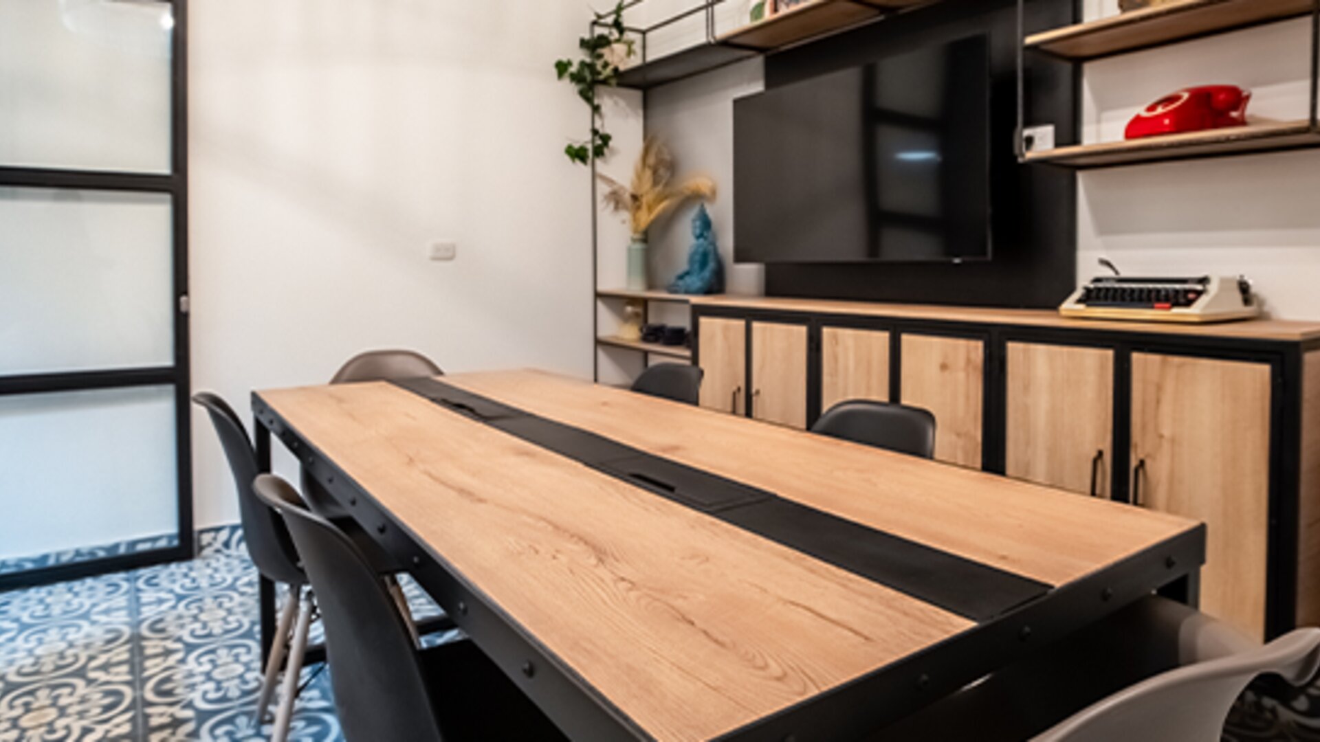 Meeting and seating area at 103 Wonderful House featuring a large wooden table, chairs, flat-screen TV and modern shelving.