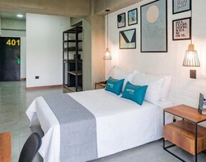 Spacious guest room at Hotel Loft 32 featuring a comfortable bed, bedside tables, wall-mounted TV and modern artwork.