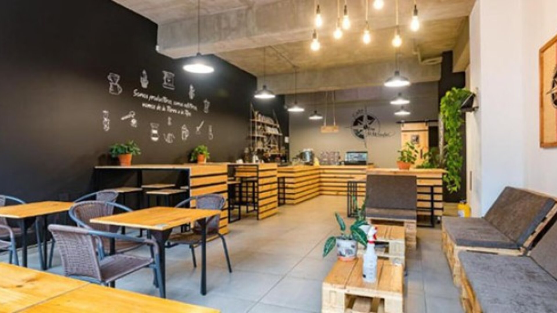 Café-style dining area at Hotel Loft 32 featuring wooden tables, lounge seating, greenery and modern lighting.