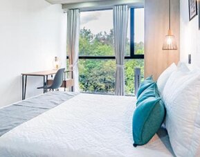 Bright guest room at Hotel Loft 32 featuring a comfortable bed, workspace and large window overlooking greenery.