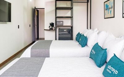 Spacious guest room at Hotel Loft 32 featuring two beds, teal accent cushions, a flat-screen TV and in-room storage.