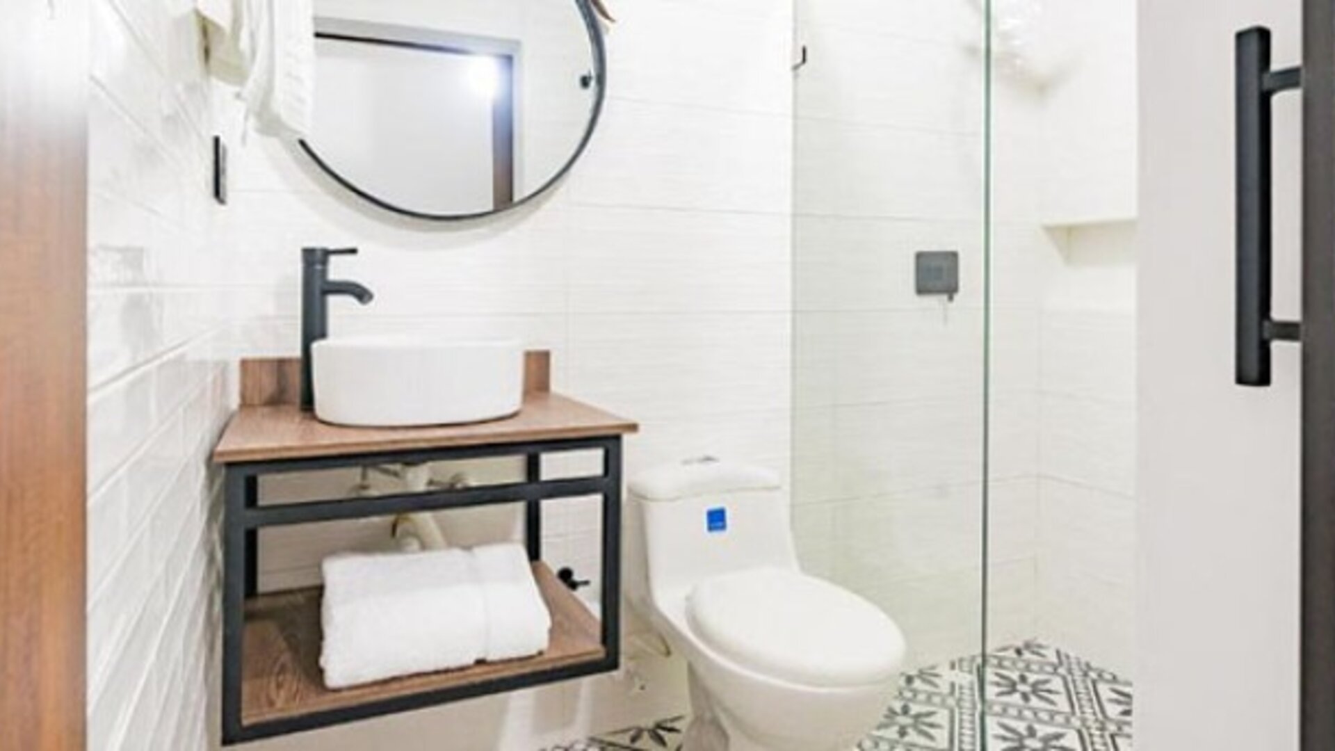 Modern bathroom at Hotel Loft 32 featuring a vessel sink, round mirror, toilet and glass-enclosed shower.