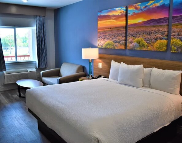 King room at Days Inn & Suites By Wyndham Downtown/University Of Houston featuring a king bed, seating area, window and colorful landscape artwork.