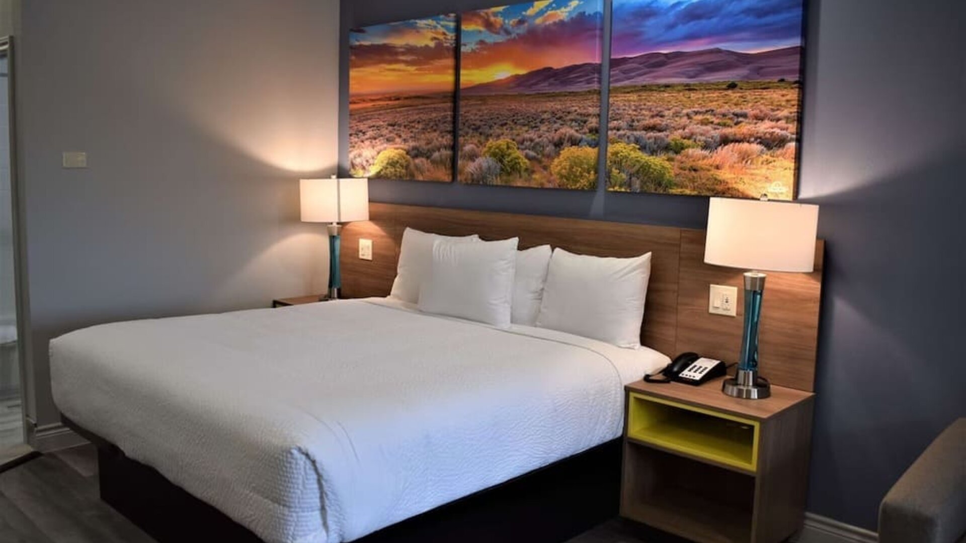 Guest room at Days Inn & Suites By Wyndham Downtown/University Of Houston featuring a king bed, bedside lighting and colorful landscape artwork.