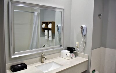 Bathroom vanity at Days Inn & Suites By Wyndham Downtown/University Of Houston featuring a large mirror, sink, hair dryer and countertop amenities.