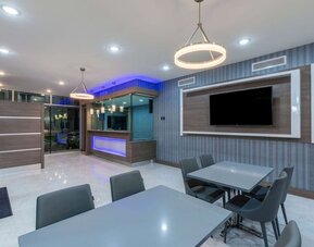 Lobby area at Days Inn & Suites By Wyndham Downtown/University Of Houston featuring dining tables, modern lighting and a wall-mounted TV.