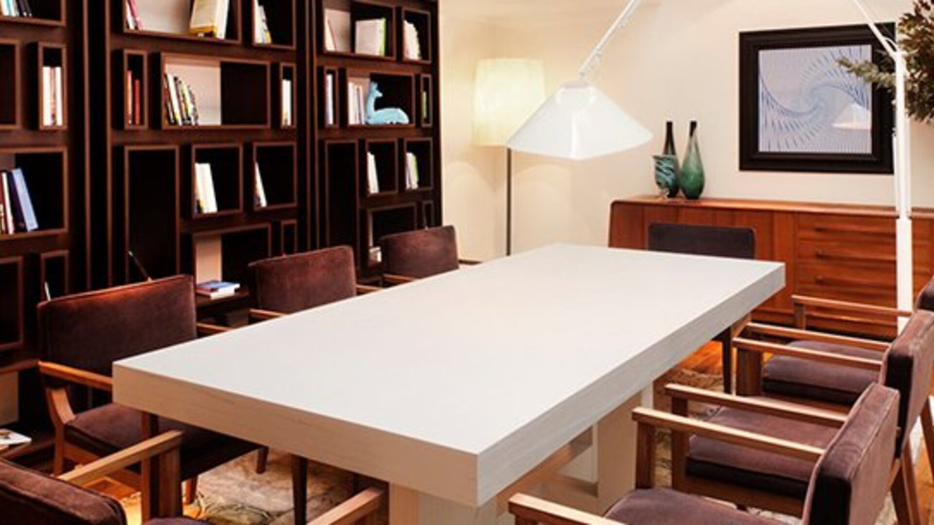Meeting room at Hotel Pulitzer Buenos Aires featuring a large central table, upholstered chairs, bookshelves and contemporary lighting.