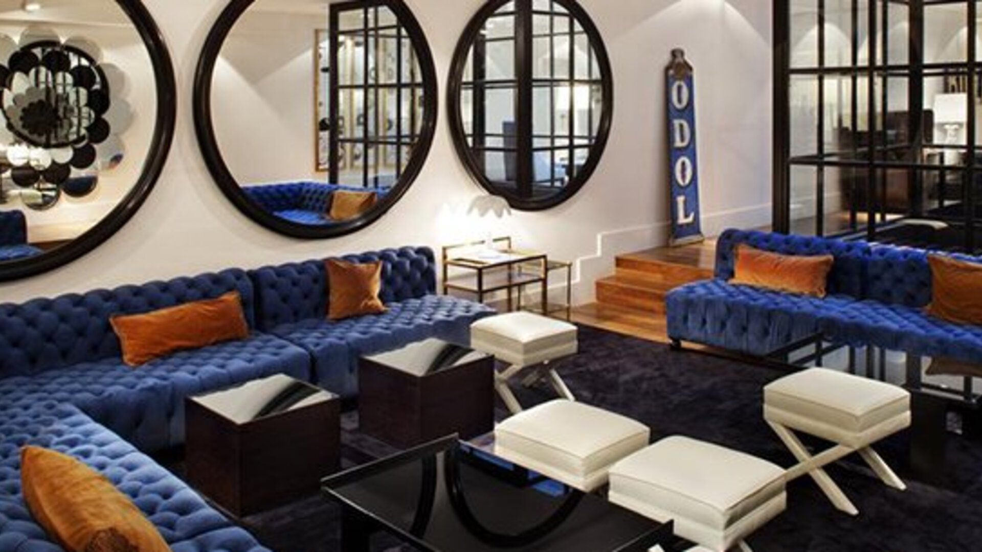 Lobby lounge at Hotel Pulitzer Buenos Aires featuring deep blue sofas, white ottomans, large round mirrors and modern furnishings.