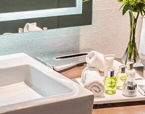 Bathroom vanity at NH Collection Mexico City Centro Histórico featuring a modern sink, illuminated mirror, fresh towels and guest amenities.