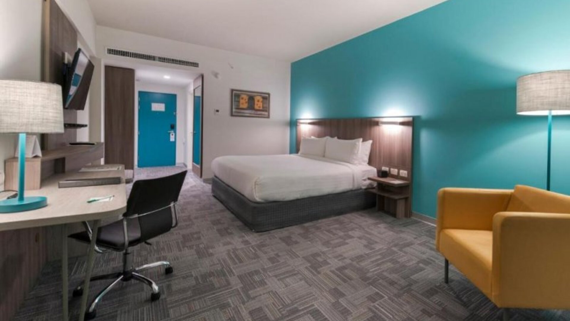 Guest room at Holiday Inn Lima Airport featuring a king bed, work desk, armchair, television and contemporary turquoise accent wall.