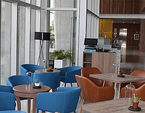 Dining area at Holiday Inn Lima Airport featuring colorful seating, café-style tables and floor-to-ceiling windows.