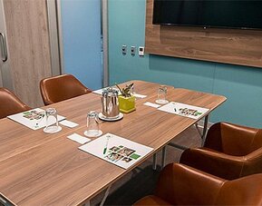 Meeting room at Holiday Inn Lima Airport featuring a conference table, leather chairs, presentation materials and a wall-mounted screen.