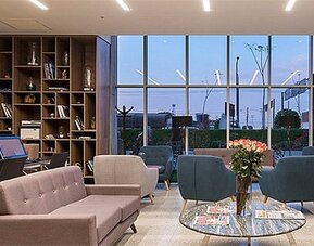 Lobby area at Holiday Inn Lima Airport featuring contemporary sofas, armchairs, bookshelves and floor-to-ceiling windows.