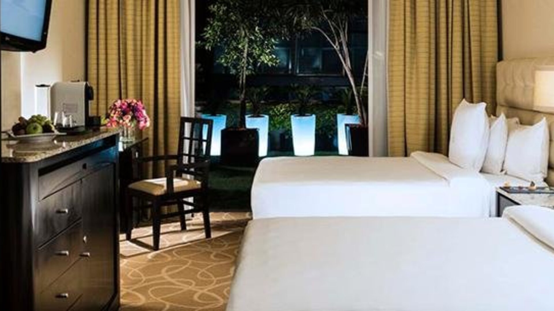 Guest room at Hotel Marquis Reforma featuring two beds, a work desk and floor-to-ceiling windows overlooking an outdoor area.