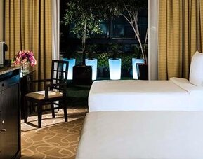 Guest room at Hotel Marquis Reforma featuring two beds, a work desk and floor-to-ceiling windows overlooking an outdoor area.